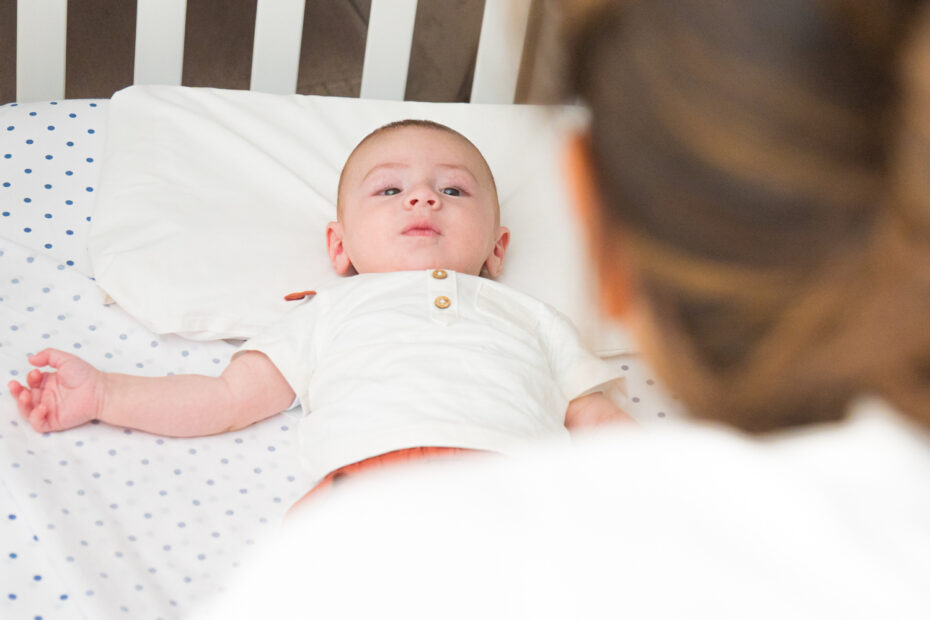 Un bambino sdraiato su un lettino, guarda verso una figura adulta che si intravede di spalle.