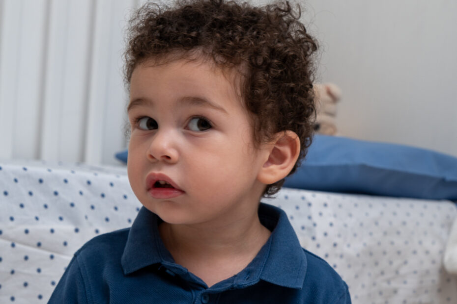 Un bambino seduto vicino a un letto sfoglia un libro illustrato con immagini colorate di insetti e pianeti.